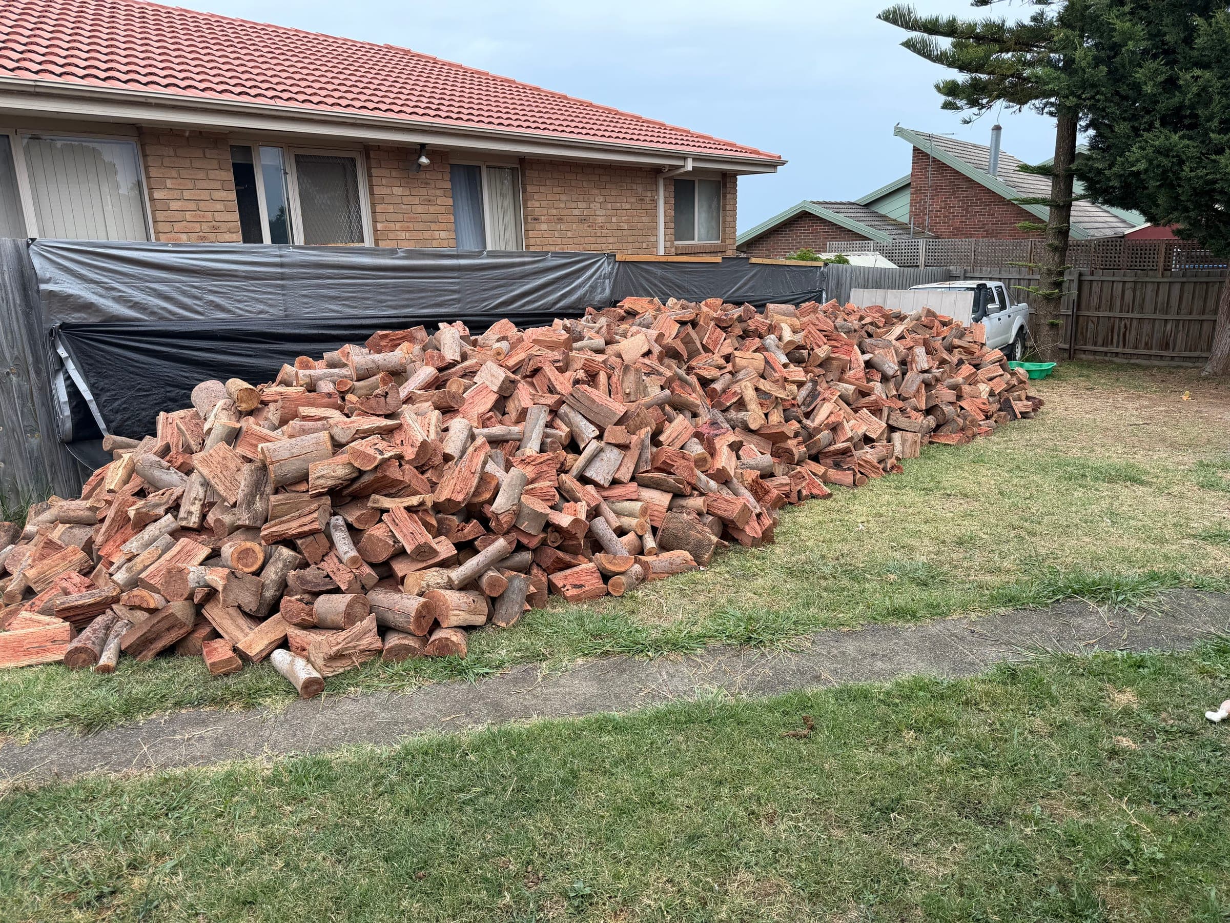 A large split firewood delivery stacked in front of a residential property