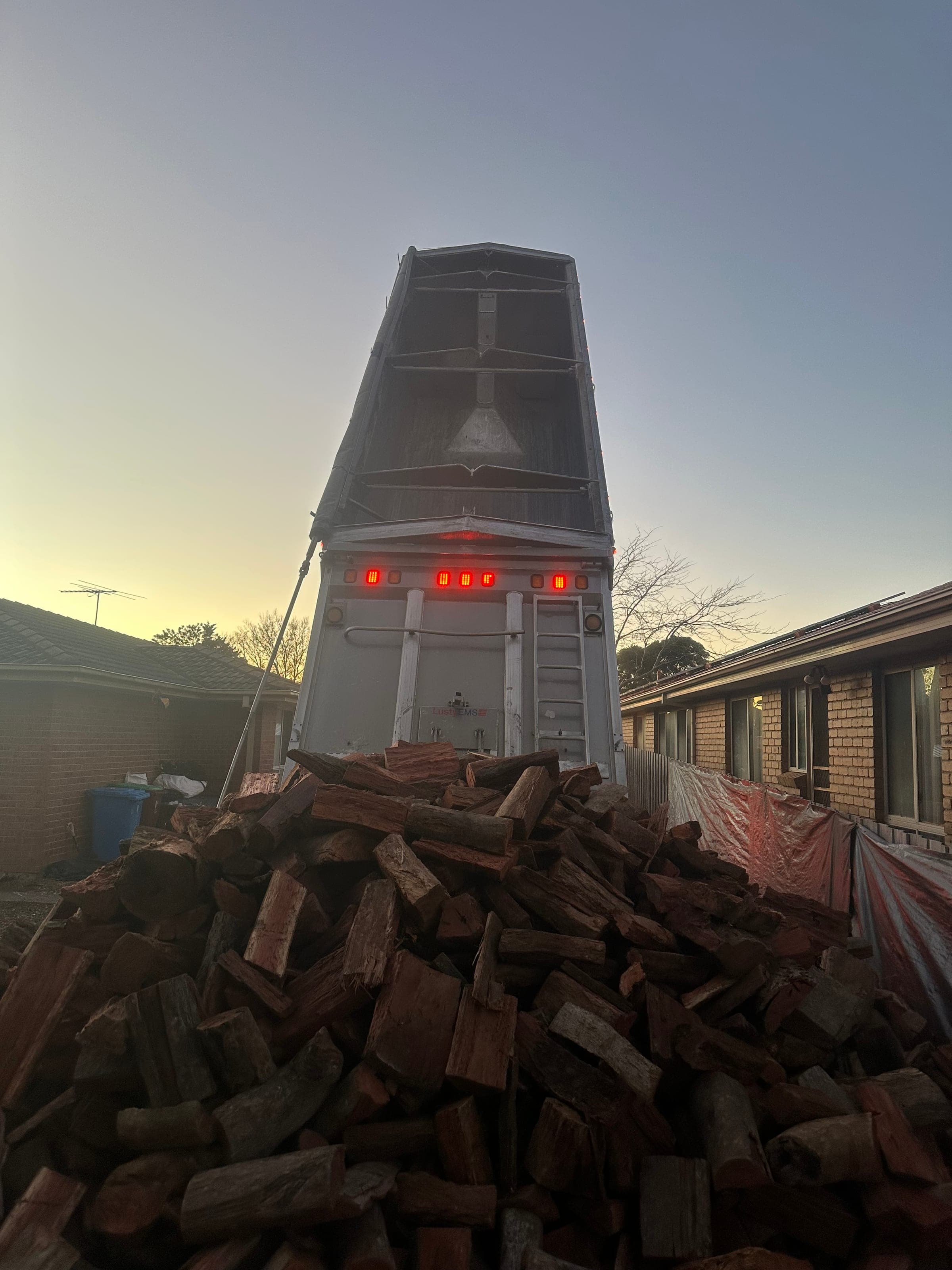 A tipper trailer raised at sunset, dropping a bulk firewood load